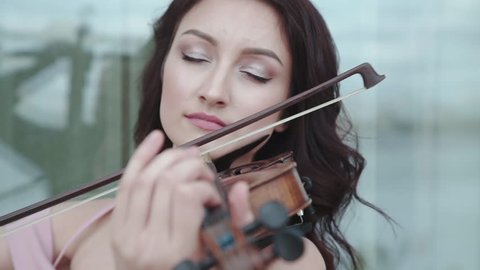 Passionate woman enthusiastically playing on the violin at building. Slowly