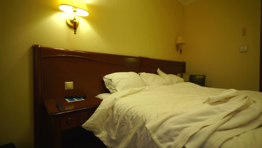 White bathrobe on unmade double bed in hotel room lit by lamps with warm golden light