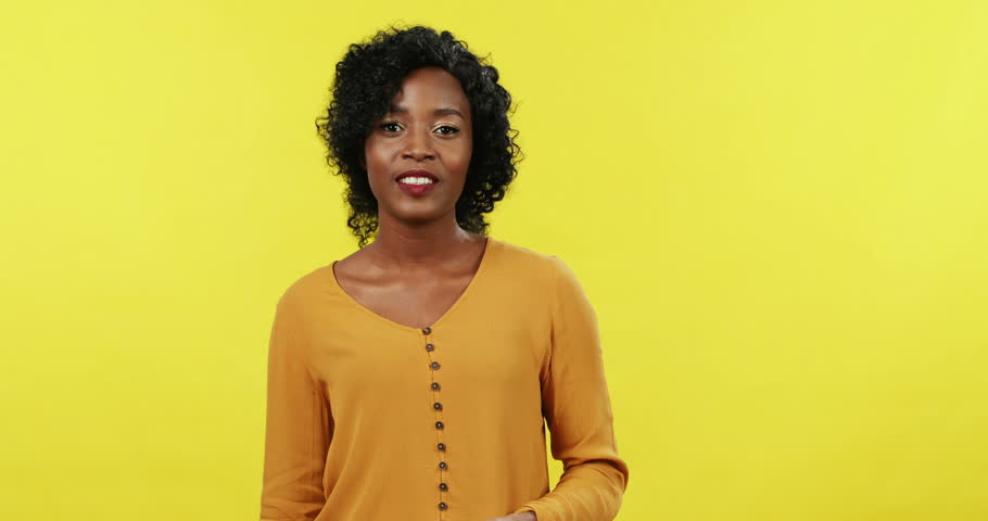 Portrait of the young attractive African American woman posing and smiling to the camera with packets after shopping. Yellow background.