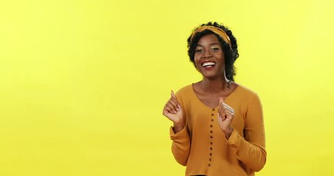 Young African American happy pretty woman dancing and moving funny on the yellow background.
