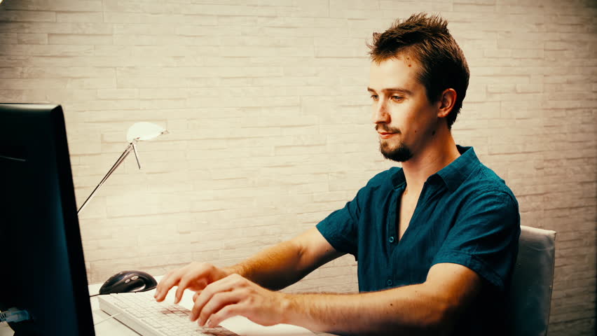 Internet troll pissed off fall back while typing. Static medium shot of a man in focus sitting behind the computer and fast typing.