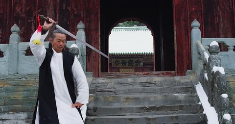 Asian master, demonstrates Tai chi martial arts sword combat in Wudang mountain China. Slow motion, red cinema camera. Note: Chinese symbols, Taoism, practice has a purpose don't forget core belief.
