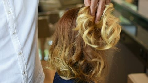 Hairdresser gives final touch to beautiful red hair of Caucasian young woman