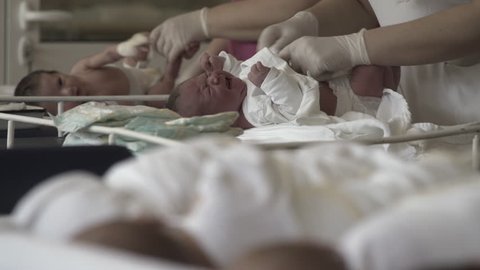 Hands in surgical gloves of midwives or nurses while  changing diapers 
 crying newborn babies on table at hospital maternity ward.Close up.Shallow depth of field.
