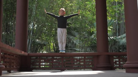 A little Chinese girl wearing black clothes white trousers jumping down the ground, opening arms, splitting her leg hair flying in the mid air