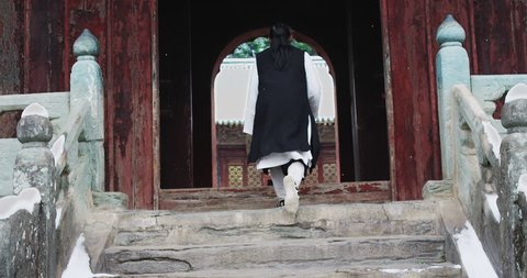 Asian master of tai chi martial arts walking through archway in Wudang mountain China. Slow motion, red cinema camera. Note: Chinese symbols, Taoism, practice has a purpose don't forget core belief.