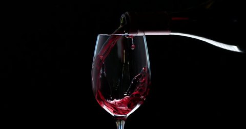 Hand pouring wine into the glass. Slow motion of spilling alcohol over black background. RED camera