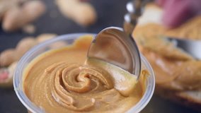 Peanut butter. Creamy smooth peanut butter in jar on a table. Spoon on Natural nutrition and organic food. American cuisine. 4K UHD video, slow motion