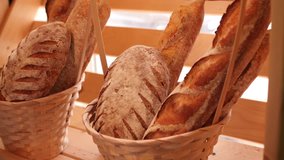 Breads and other baked goods in decorative baskets on wooden bakery store shelves in background slow motion medium shot in 4K