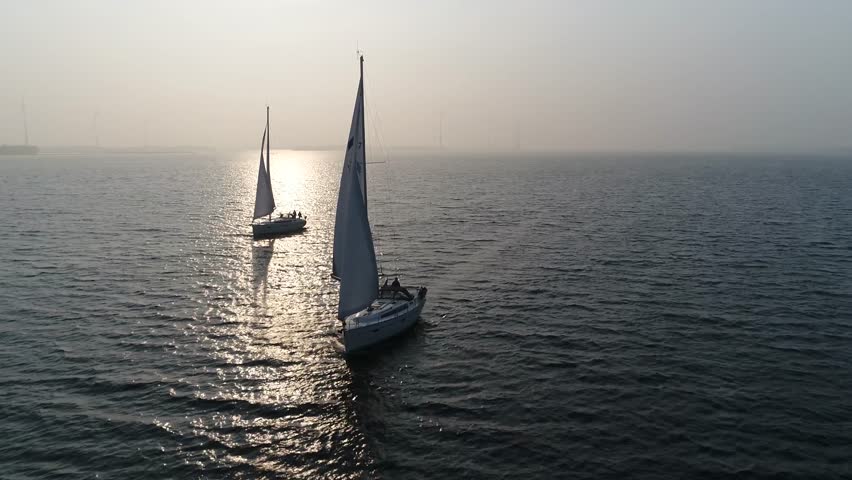 Aerial view of two sloops at sundown are sailing boats with single mast and fore-and-aft rig plus one head-sail the most common setup of modern sailboats is the Bermuda-rigged configuration 4k quality Royalty-Free Stock Footage #1027128272