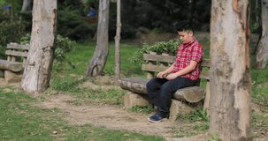 Portrait of a preteen boy with digital tablet computer sitting on a bench at summer park. Kid watching to screen, reading, typing, playing games. Technology, internet communication and people concept 