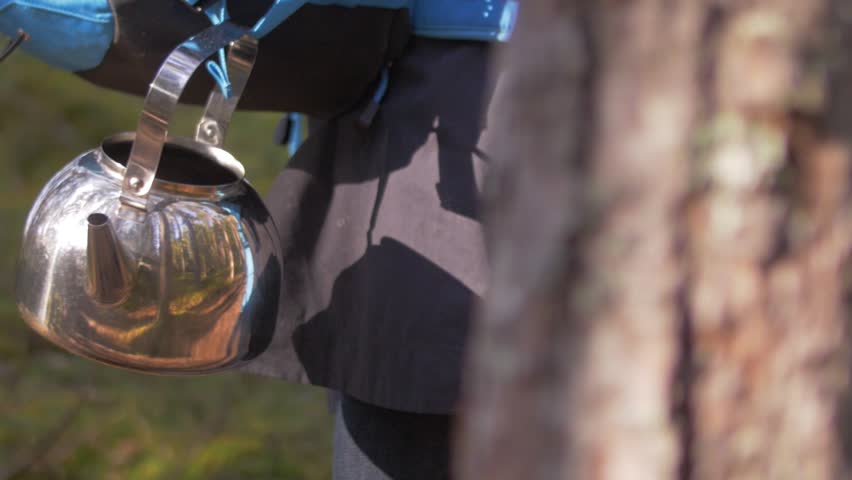 Metal shiny tea pot with reflection of the forest and autumn slow motion atmosphere, blue tourist bag, through trees
