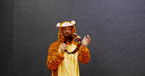 half body shot of a funny smiling man wearing onesie kigurumi, tiger costume and playing tambourine, very funny attitude for a professional musician. onesie, costume, onesies