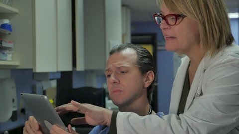 Male and female physicians looking at a digital tablet and discussing a case together in a modern medical clinic or hospital in slow motion