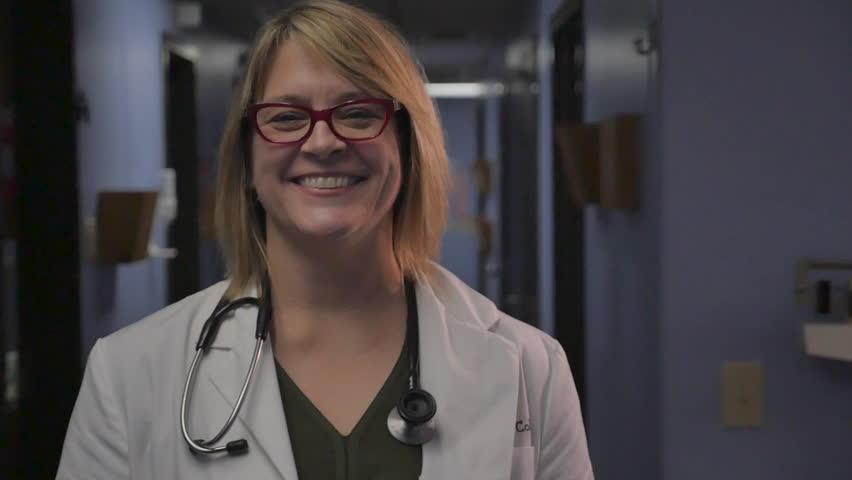 Attractive woman doctor crossing her arms and smiling at camera while standing in a hospital or medical clinic hallway - slow motion dolly shot | Shutterstock HD Video #1027148834