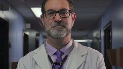 Portrait of a handsome, sophisticated, male doctor with a stethoscope around his neck smiling, nodding his head yes, and looking at the camera in a clinic or hospital in slow motion