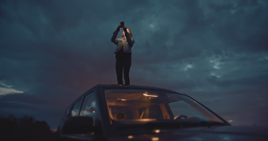 Slow Down To Enjoy Your Trip, Traveler woman takes pictures at night on smartphone device while standing on the roof of the car, Connection in Mountains, Cinematic Shot Royalty-Free Stock Footage #1027149923