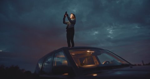 Slow Down To Enjoy Your Trip, Traveler woman takes pictures at night on smartphone device while standing on the roof of the car, Connection in Mountains, Cinematic Shot