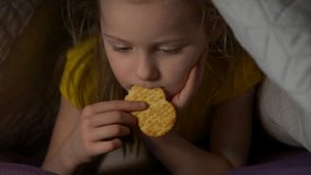 Little girl eat at night watching cartoons video eating cracker snack lying on the bed with smartphone child little girl caucasian white european 5 years old in yellow t shirt smartphone addiction