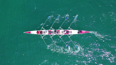 Aerial drone bird's eye view video of red sport canoe operated by team of young men and women in emerald clear sea