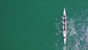 Aerial drone top down video of sport canoe operated by team of young men and women in open ocean sea