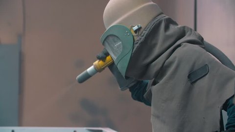 worker wearing mask using sand blast on metal surface in workshop