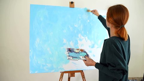 Woman artist begins to paint a picture with blue acrylic paints with a spatula