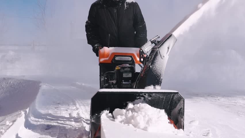 A man cleans the snow with a snowblower during a snowfall. Slow motion.
