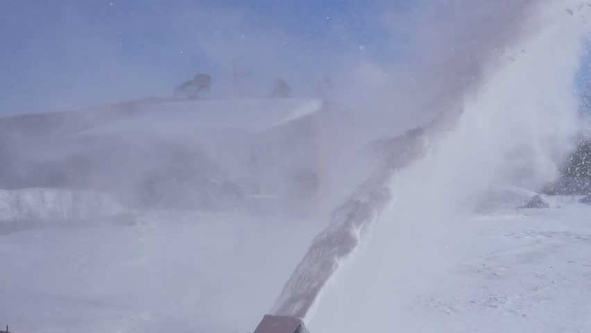 A man cleans the snow with a snowblower in sunny winter weather.