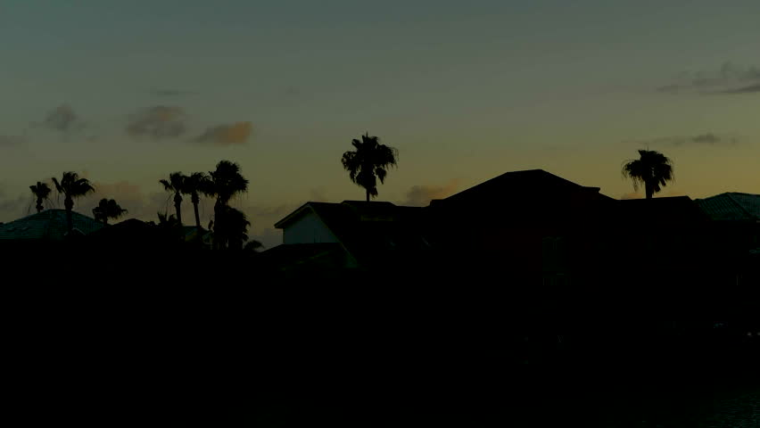 Sunset off the Texas coast behind silhouetted houses and trees.
