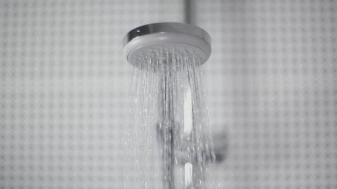 Close-up of turning on and off shower head in bathroom, white tiles with black pattern on the walls, water flow in front of camera, falling drops in slow motion