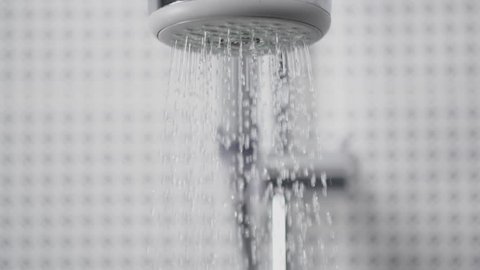 Close up of turning on and off the shower head in bathroom, white tiles with black pattern on the walls, water flowing slowly in front of camera, falling drops shot in slow motion 200 fps