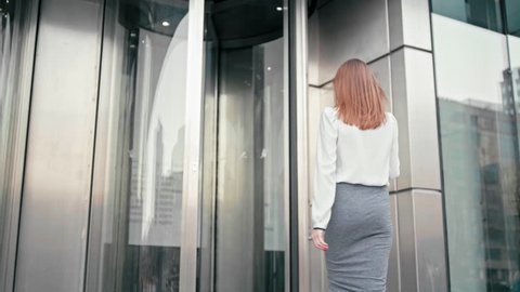 Anonymous Slender Caucasian Business Woman Manager in White Shirt is Entering into Office Building via Glass Revolving Door. Back View Low Angle 4K Slow Motion Corporate Shot