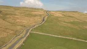 Aerial drone video, motorcycle on remote uphill winding country road amid moorland: Kidstones Bank near Cray, Yorkshire Dales, England, UK
