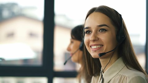 4K. Two young smiling women operators answer client. Office call center work process.  