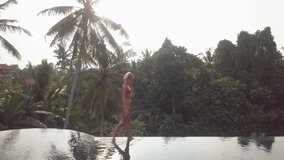 Drone aerial view of Young woman by the edge of an infinity pool in Bali enjoying tropical climate vacations in Asia.
Girl balancing on the edge of water in rainforest, holidays 
