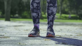 Medium shot of young female legs in floral leggings and hands fixing laces on running shoes. Sport concept