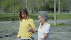 Smiling young woman in yellow sweatshirt and excited middle-aged woman with grey hair in white T-shirt making high lunge exercise, changing legs, supporting each other. Sport concept