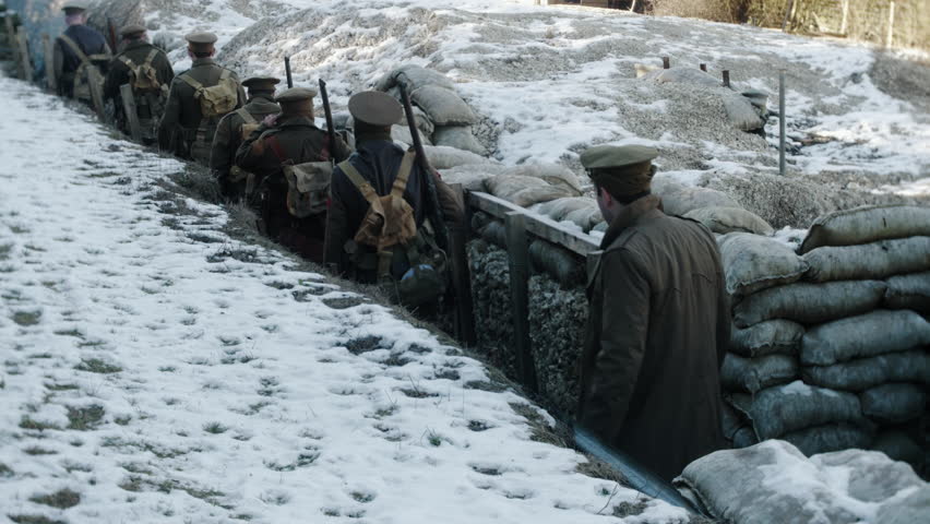 soldiers walk through a trench towards the front line. Snow covered sandbags line the wall of the WW1 trench.
