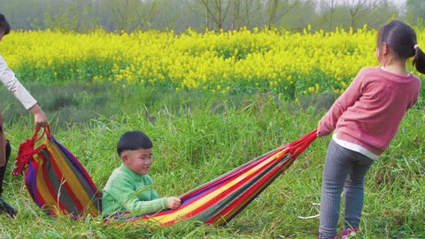 Cute and lively Asian kids kneeling on the grass land playing on the hammock with much fun enjoying relaxing and free sunny spring days