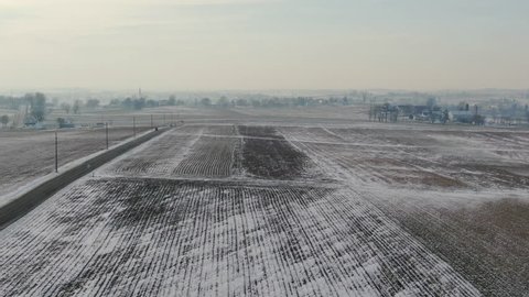 Aerial shot - Flying over snow covered farmlands. Shot in Intercourse, Pennsylvania in wintertime. A beautiful snow covered rural town with farms, meadows, farmlands and a small village center.