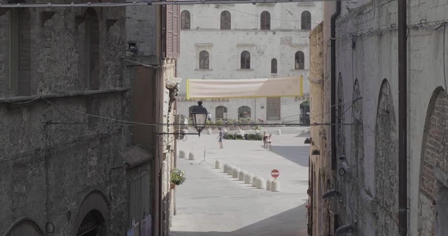 Looking down onto Piazza del Popolo, a city square in Todi, Italy through the buildings as people walk by