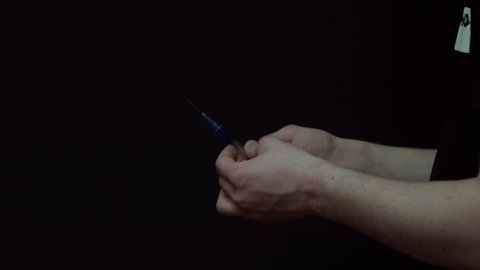 Closeup of a young man preparing a blue liquid shot and then pricking it into the vein. Isolated on black.