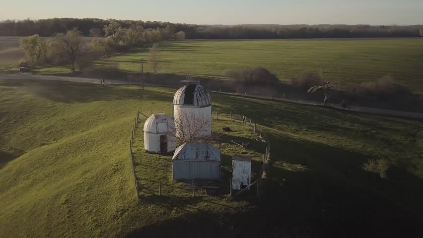Drone shot circling an old observatory, with green grass and a fence surrounding it.