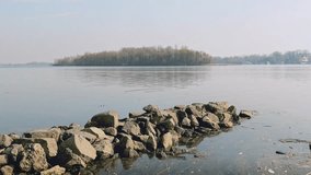 Pontoon made of rocks close to the Dnieper river in Kiev, Ukraine. A soft spring morning, mist over the fresh and calm water. The landscape softly disappears in the distance. 4K video