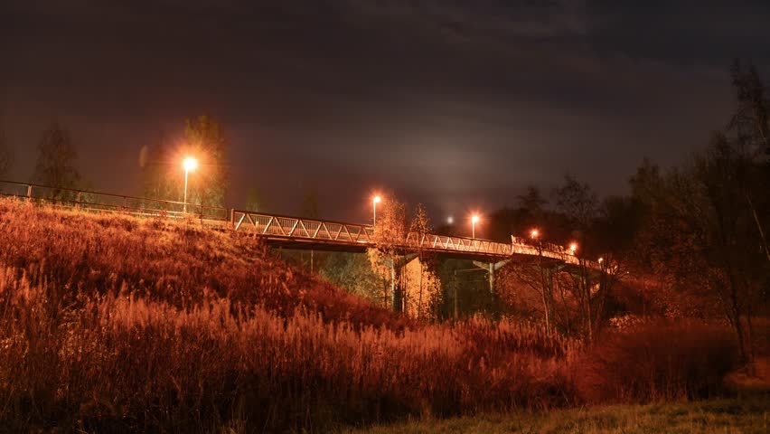 Timelapse of a bike and pedestrian bridge in tampere, a city in finland at night. Clouds are moving and moon is shining bright. A train is passing by as well