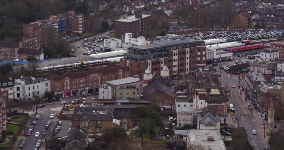 Wide aerial view tracking a commuter train passing through Surbiton train station, London, UK