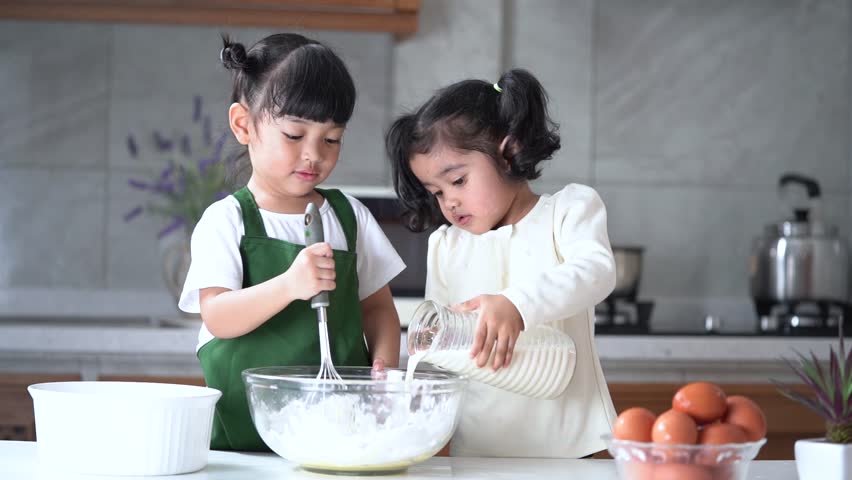 Happy Asian kids are preparing the dough, bake cookies in the kitchen. (Video slow motion)