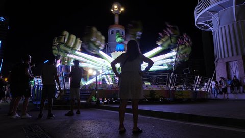 BARCELONA, SPAIN - AUGUST 20, 2018: People enjoy ride at techno jump attraction, woman stand hands on hips, looking to spinning and bouncing carousel. Temporary fair at festival time on city street