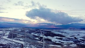 Video descending to a black road at sunset on a snow covered mountain ridge with a line of wind turbines silhouetted against the evening sky, central Spain, Avila.  
